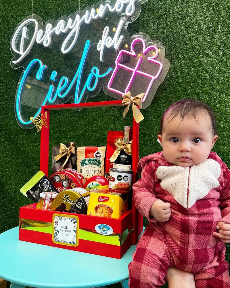 Bebé junto a una ancheta navideña decorada con moños rojos